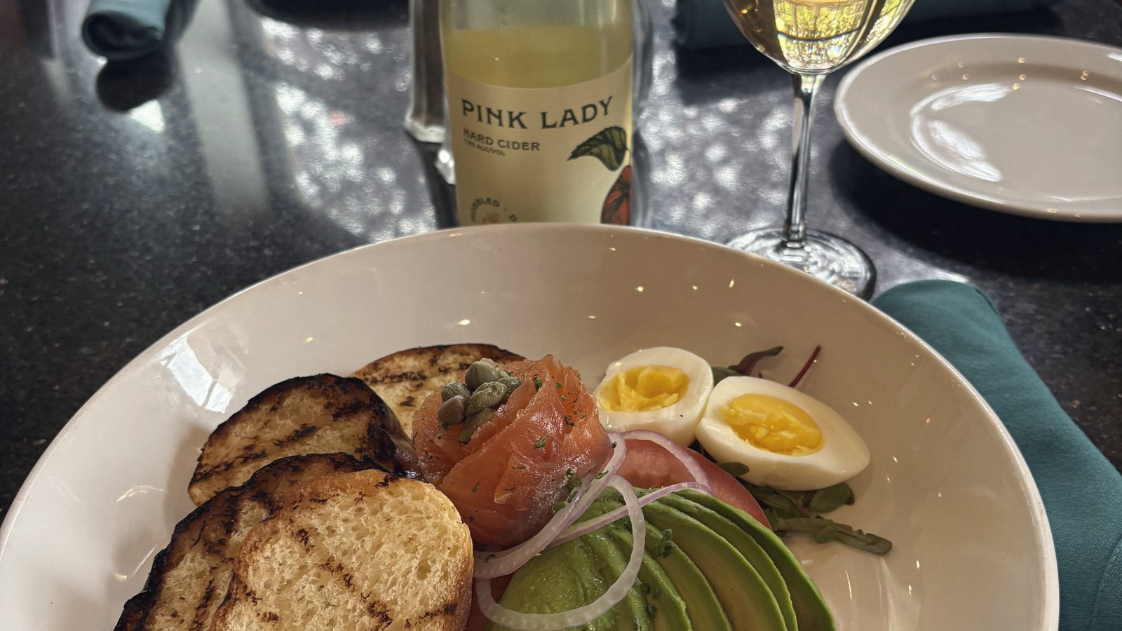 A bread and cheese plate with a wine bottle and glasses behind. Shallow depth of field.