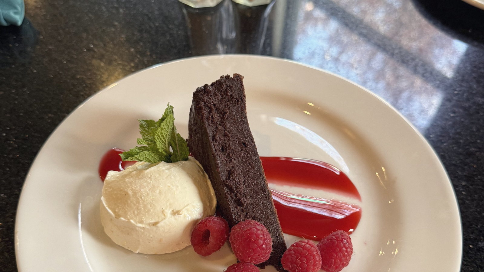 A chocolate and raspberry plated dessert on a dark table.